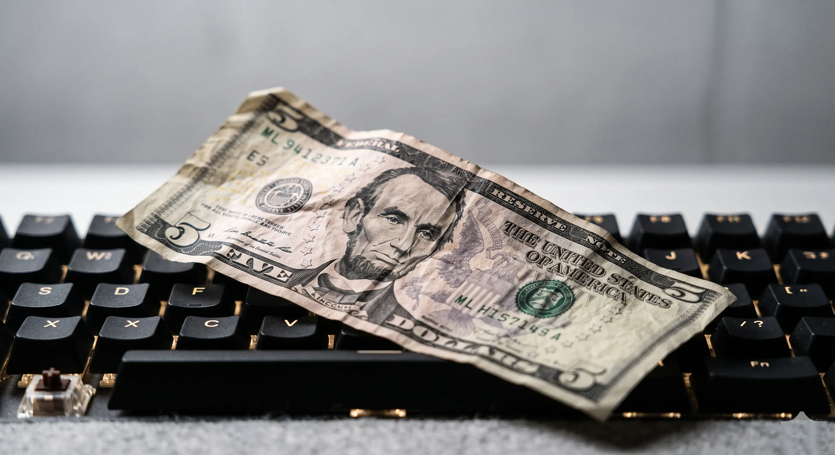A crumpled five dollar bill resting on a mechanical keyboard — representing how a $5 domain purchase exposed a critical 9.4 CVSS vulnerability in Salesforce Agentforce